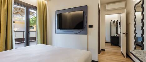 Habitación de hotel con cama, televisor montado, baño con espejo y vista al exterior.
