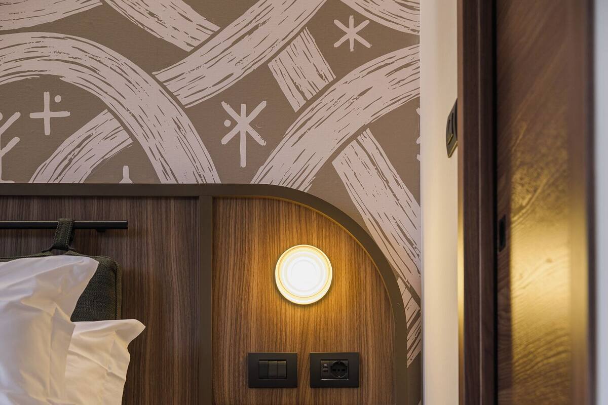 Une petite pièce compacte, dotée d’un lit, d’une lampe fixée au mur et d’un lavabo au design moderne et original.