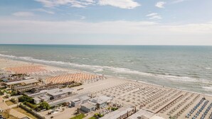 A beach with rows of umbrellas and sun loungers, a parking area, and buildings with signage. - MOKO LIFESTYLE HOTEL-Nuova apertura 2026 (Milano Marittima)