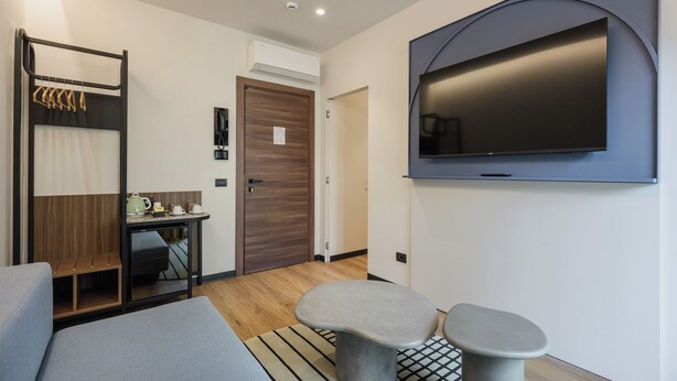 A modern hotel room with a flat-screen TV, a seating area with a sofa and two stools, a small table with a kettle, and a coat rack. - MOKO LIFESTYLE HOTEL-Nuova apertura 2026 (Milano Marittima)
