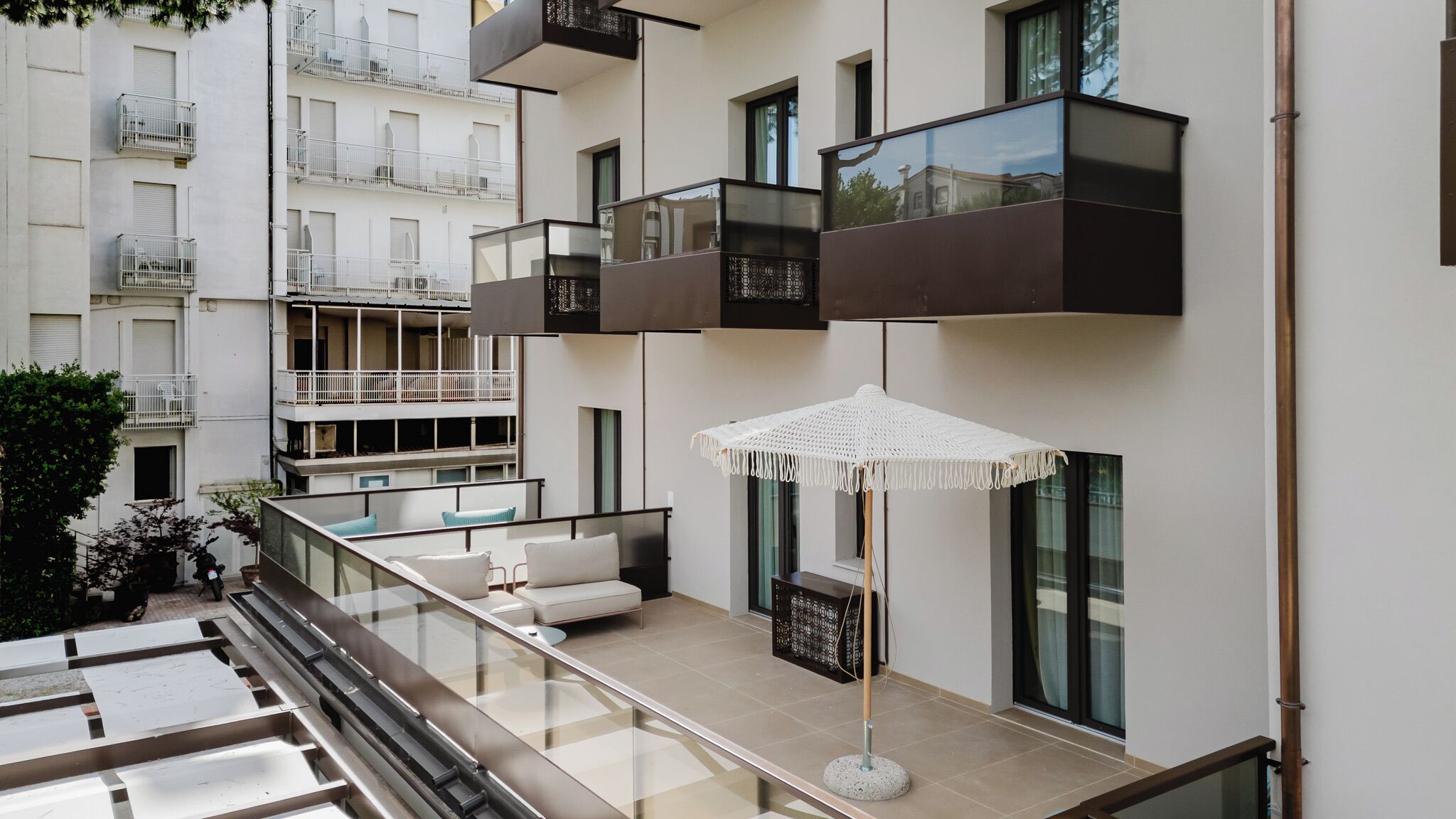 A modern apartment with a balcony, a white umbrella, and a view of neighboring buildings.