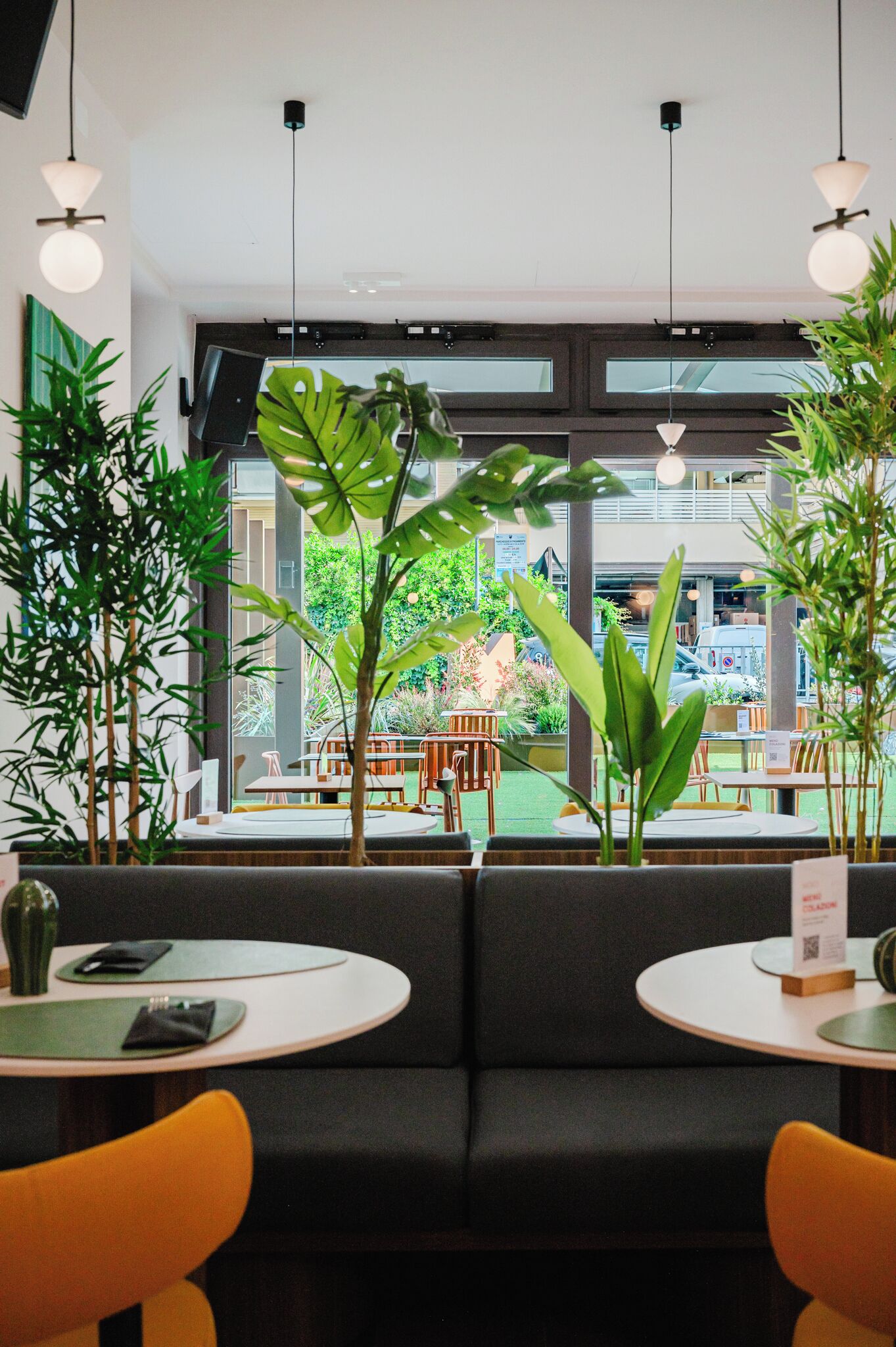 A restaurant with round tables, black cushioned seating, and hanging pendant lights.
