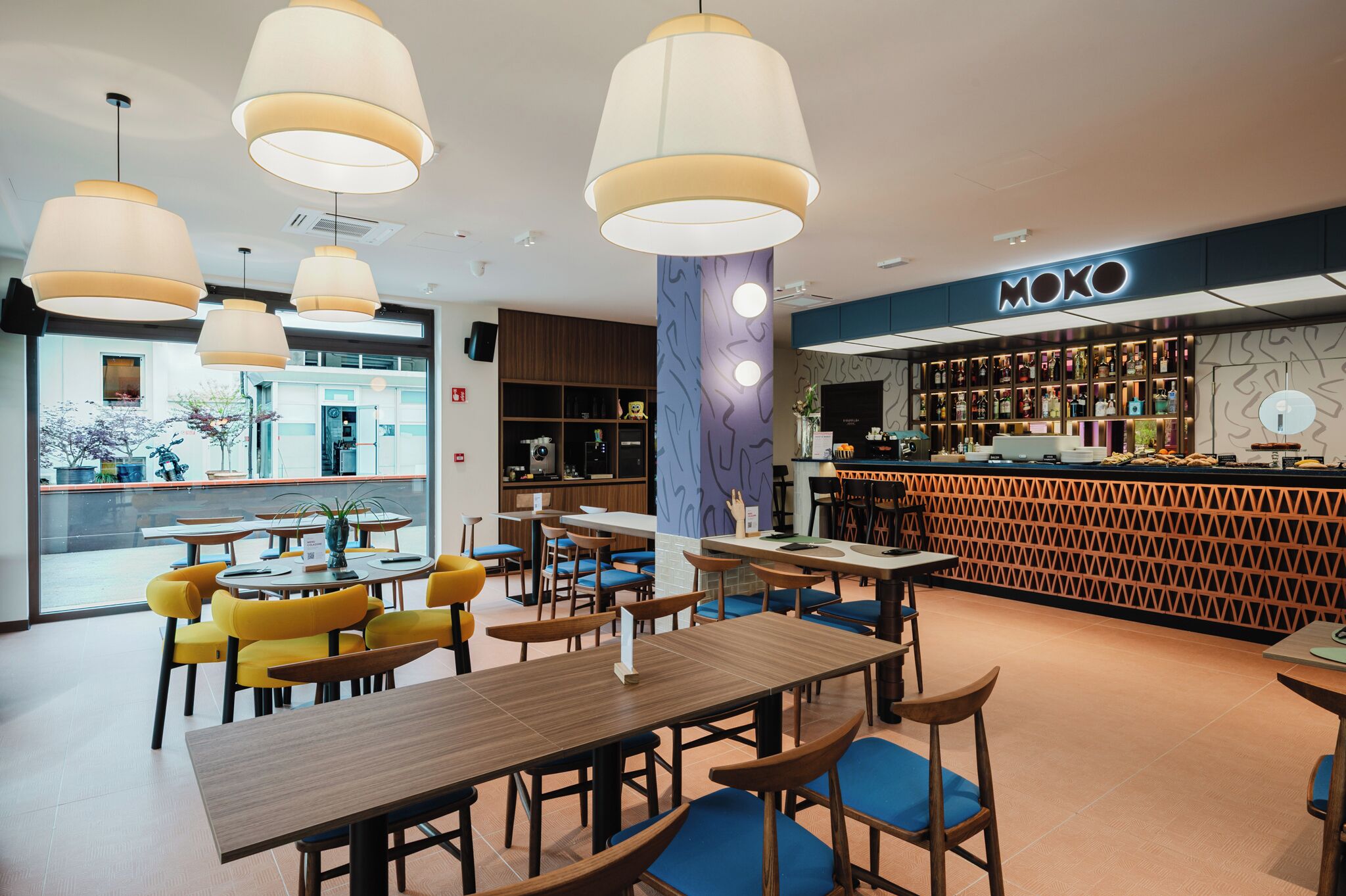 A modern cafe with yellow chairs, wooden tables, and pendant lighting.