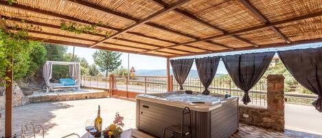 A covered outdoor area with a hot tub, seating, and a view of the landscape.