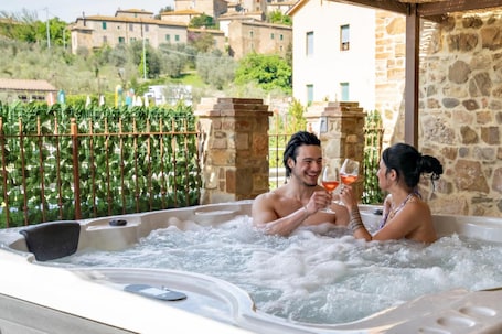 A hot tub with two people, surrounded by stone walls and greenery.. Sant'Antimo Montalcino Holiday Home with Garden View and Private Parking