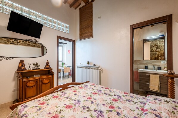 Un dormitorio con cama, cómoda, espejo, televisor y baño con lavabo y espejo.