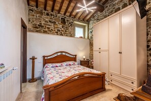 A bedroom with a wooden bed, a stone wall, a wardrobe, and a ceiling light fixture. - Sant'Antimo Montalcino Holiday Home with Garden View and Private Parking (Montalcino)