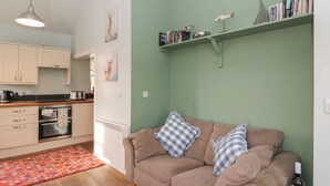 A cozy living room with a beige sofa, a patterned rug, and a bookshelf with books and decorative items. - Ardpatrick South Lodge (Tarbert)