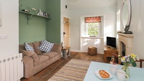A cozy living room with a brown sofa, a small table with a loaf of bread and two mugs, a fireplace, and a green wall with shelves. - Ardpatrick South Lodge (Tarbert)