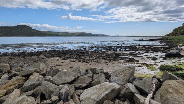 A rocky shoreline with a body of water, distant hills, and a partly cloudy sky. - Ardpatrick South Lodge (Tarbert)