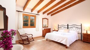 A bedroom with a bed, a rocking chair, a dresser, a mirror, and a window with curtains. - Holiday Home 'Oliveres' with Mountain View, Wi-Fi and Air Conditioning (Illes Balears)