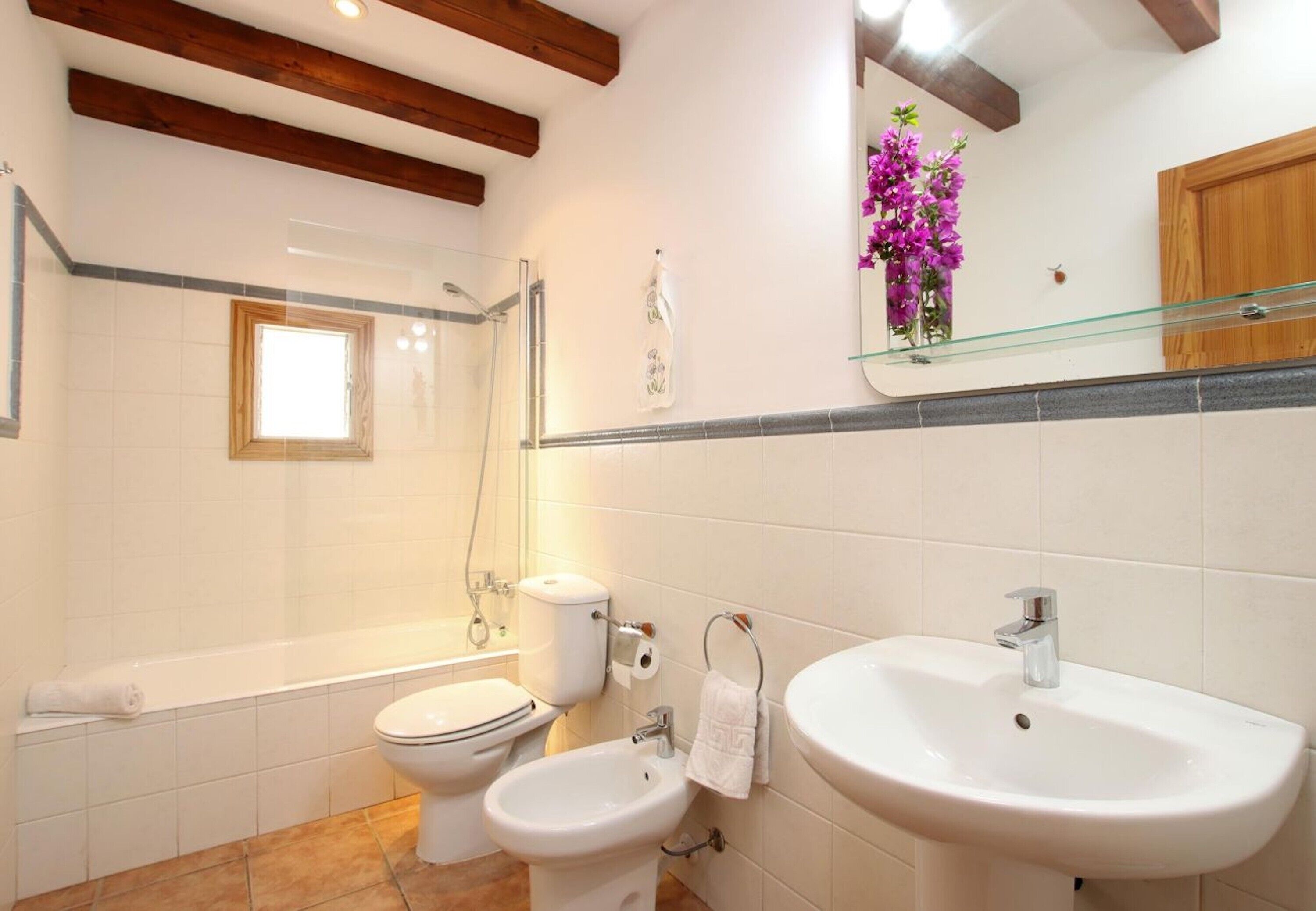 A bathroom with a bathtub, two toilets, a bidet, a sink, and a mirror with a vase of flowers.