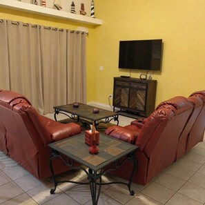 A living room with a sofa set, a coffee table, a TV mounted on the wall, and a cabinet. - Tipsy Turtle | 4BR/2 BA l Heated Pool | Sleeps 8 (Cape Coral)