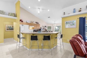 A modern kitchen with a central island, bar stools, and a dining area with a red leather chair.
