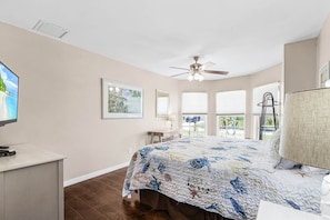 A bedroom with a bed, a desk, a television, and a ceiling fan.
