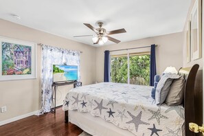 A bedroom with a bed, a ceiling fan, a TV on a stand, and a window with curtains. - Tipsy Turtle | 4BR/2 BA l Heated Pool | Sleeps 8 (Cape Coral)