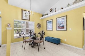 A dining area with a table and chairs, a blue bench, and wall decorations including framed pictures and a wreath.
