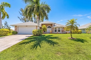 A residential house with a garage, a well-maintained lawn, and palm trees. - Tipsy Turtle | 4BR/2 BA l Heated Pool | Sleeps 8 (Cape Coral)