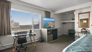 Ein Hotelzimmer mit Schreibtisch, Stuhl, Bett, Fernseher und Blick auf einen See.