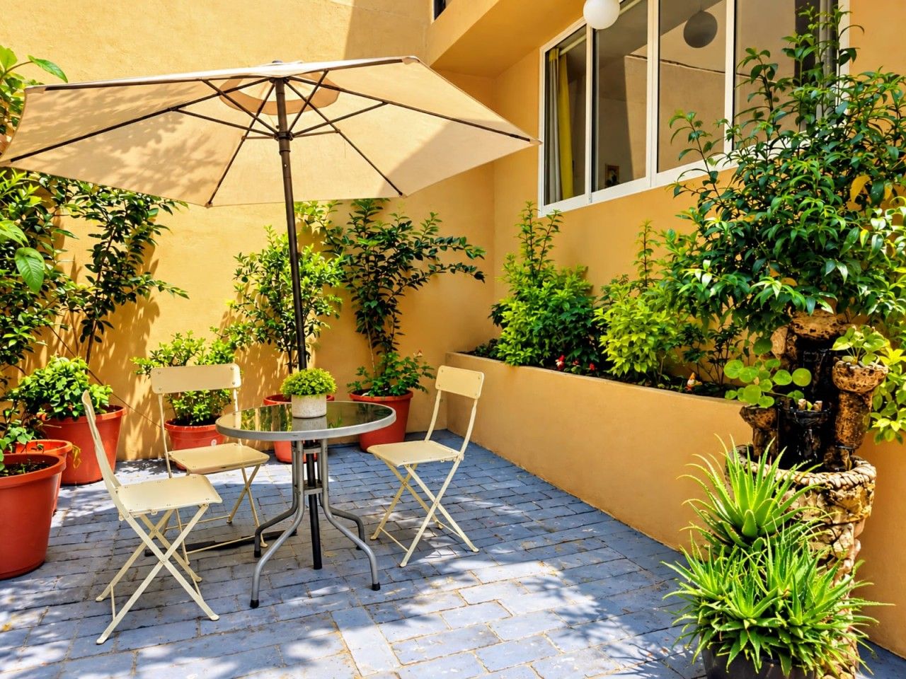 Eine Terrassengruppe im Freien mit Tisch und Stühlen, umgeben von Topfpflanzen und einem dekorativen Felsen.