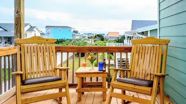 En træterrasse med to gyngestole og et lille bord, med udsigt over et boligområde med huse og have.