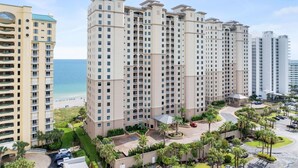 Een hoog hotel met meerdere balkons, een centrale binnenplaats en uitzicht op het strand.