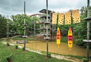 Un parco avventura all'aperto con ponti di corda, una struttura in legno e un fiume tranquillo.