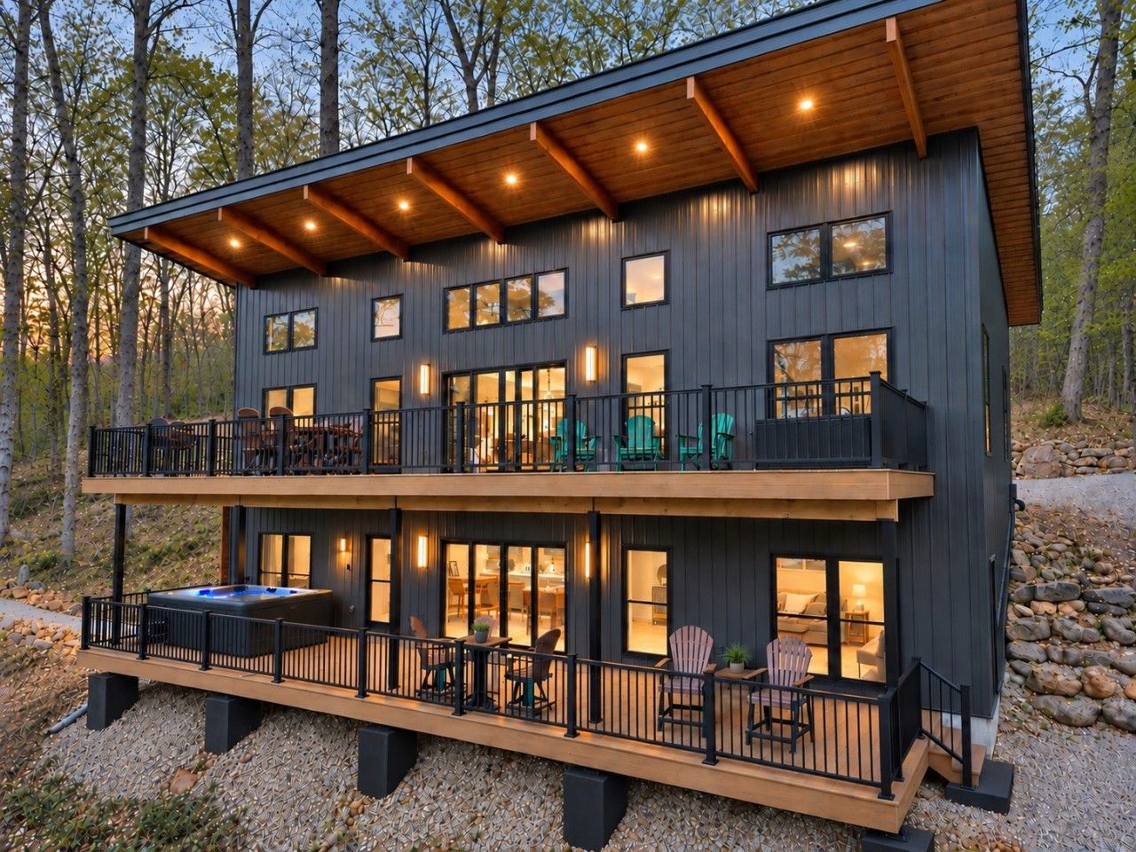 Un bâtiment à deux étages doté d’un balcon à l’étage supérieur, d’un jacuzzi au niveau inférieur et offrant une vue sur la forêt environnante.