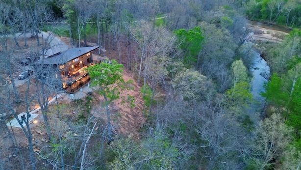 Una cabaña con terraza, rodeada de un bosque frondoso y un río.
