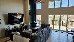 Una sala de estar con un televisor de pantalla plana grande, una chimenea de piedra, un sofá y una zona de comedor con mesa y sillas.