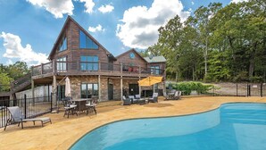 Ein großes Holzhaus mit Swimmingpool, Gartenmöbeln und einer überdachten Terrasse.