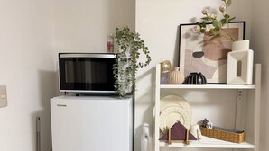 Un refrigerador blanco con un televisor encima, una pared blanca y una estantería con objetos decorativos y una cesta.