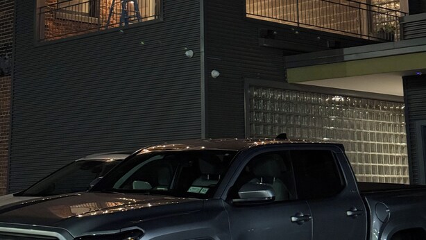 Un edificio de dos pisos con un garaje, un balcón con barandilla y luces colgantes.