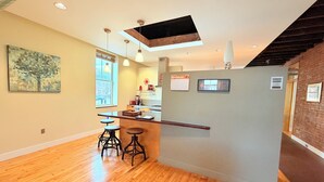 Una cocina moderna con una isla central, taburetes de bar, iluminación colgante y un tragaluz.