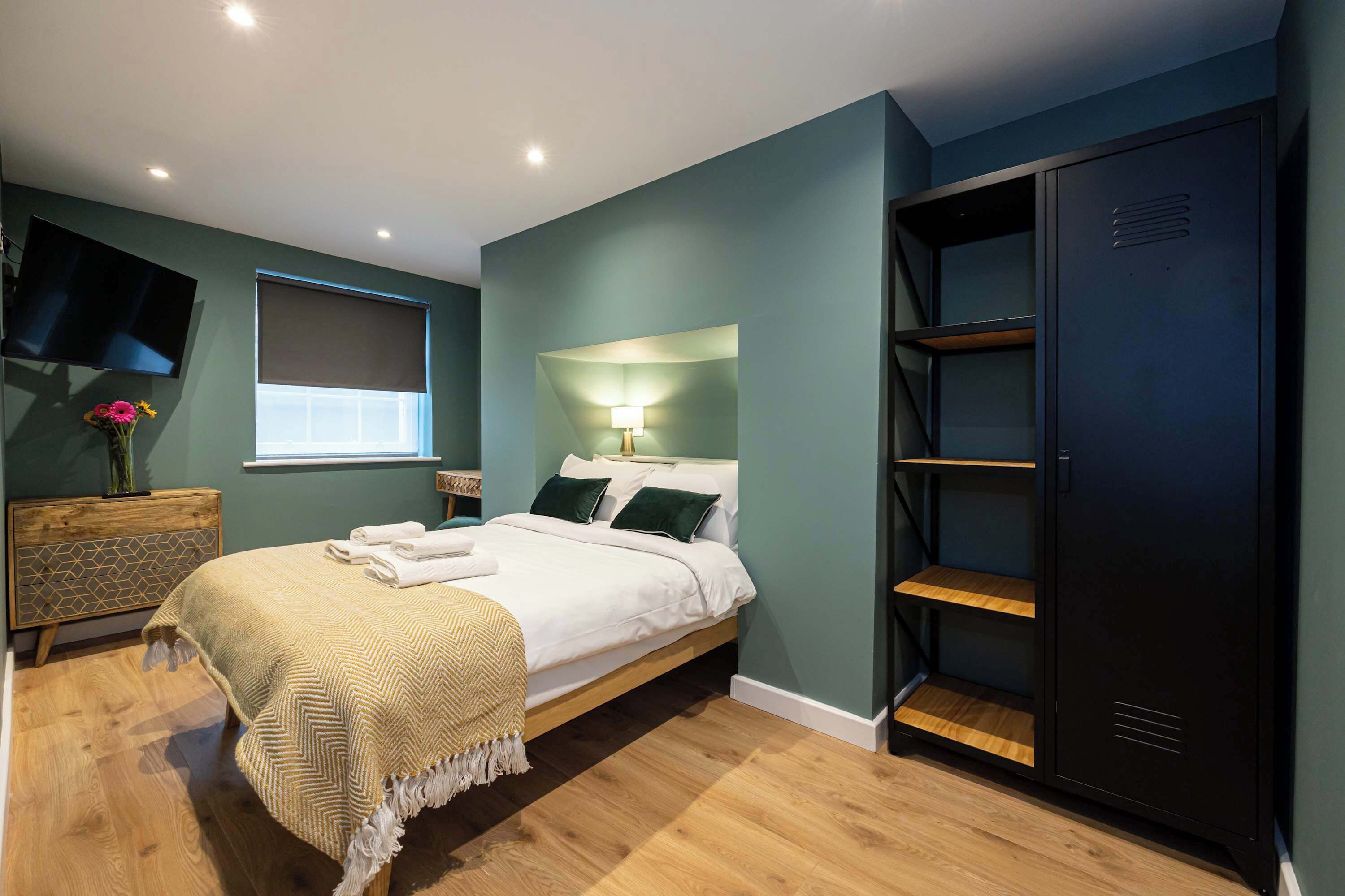A bedroom with a bed, bedside table, TV, and a wardrobe.