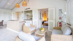 Ein großzügiger Wohnbereich mit Korbmöbeln, eine zentrale Kücheninsel mit Spüle und ein gemütliches Schlafzimmer mit Bett und Nachttisch.