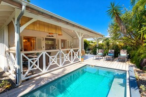 A poolside area with a covered patio, outdoor seating, and a view of the pool. - Charming Villa Grenadille and its tropical garden (Le Diamant)