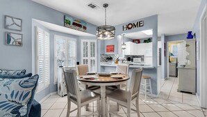A modern kitchen with white cabinets, a dining table with chairs, and a 'HOME' sign on the wall. - Best Nest (Destin)