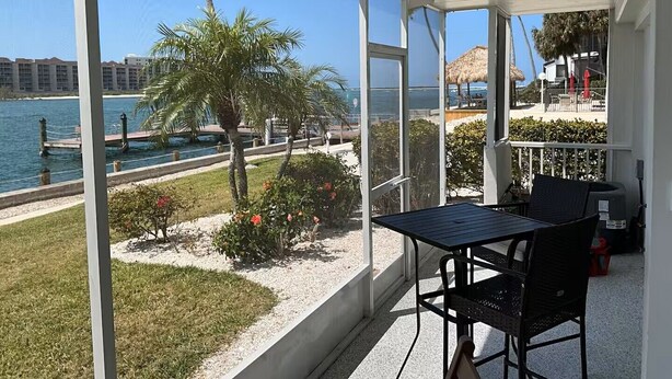 A balcony with a view of the sea, a table, chairs, and a ceiling fan. - Paradise on the Isles - Stunning Waterfront Views - Pool & Dock Steps Away (Naples)