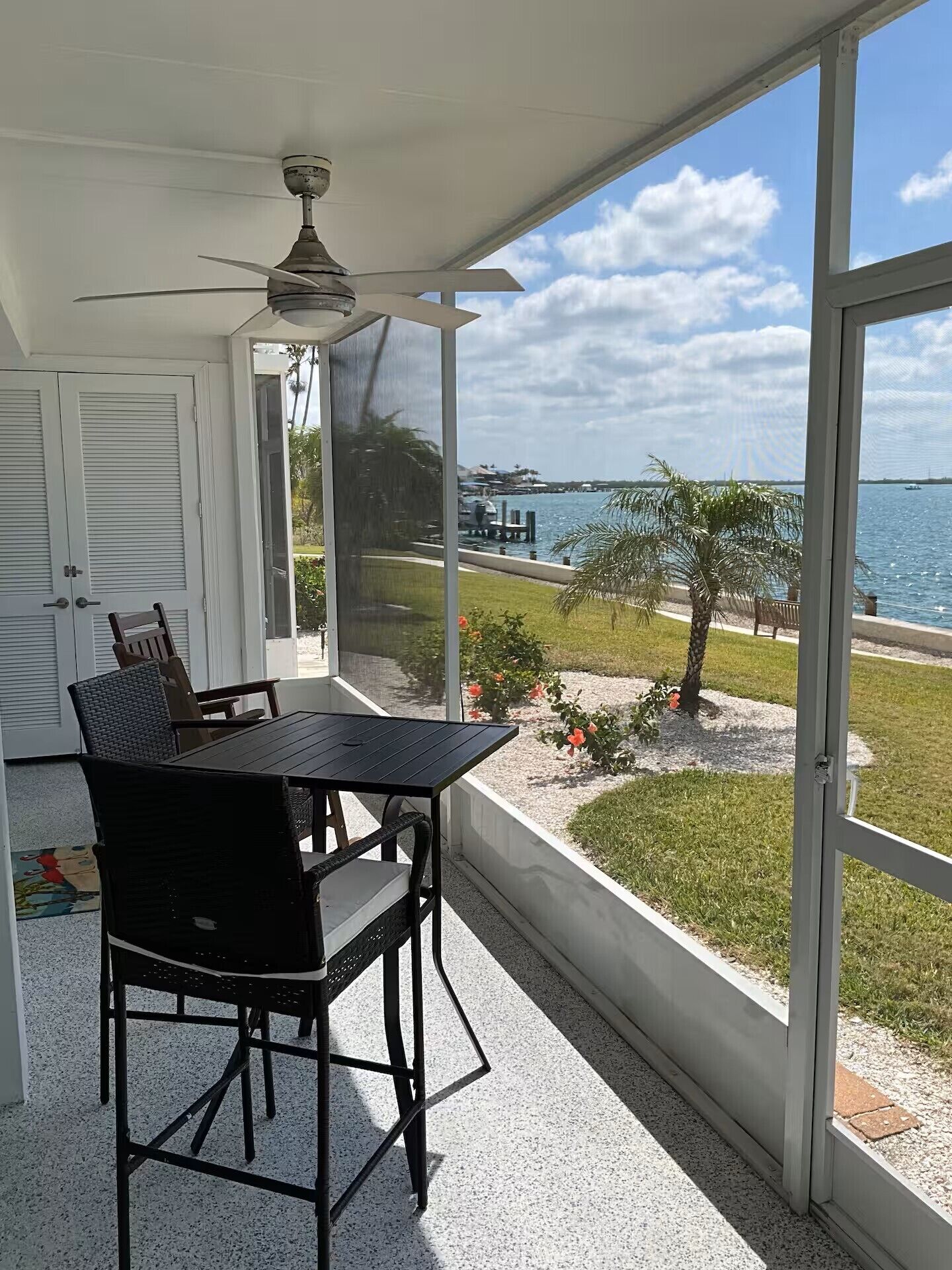 A covered patio with a table and chairs, a ceiling fan, and a view of the water and distant buildings.