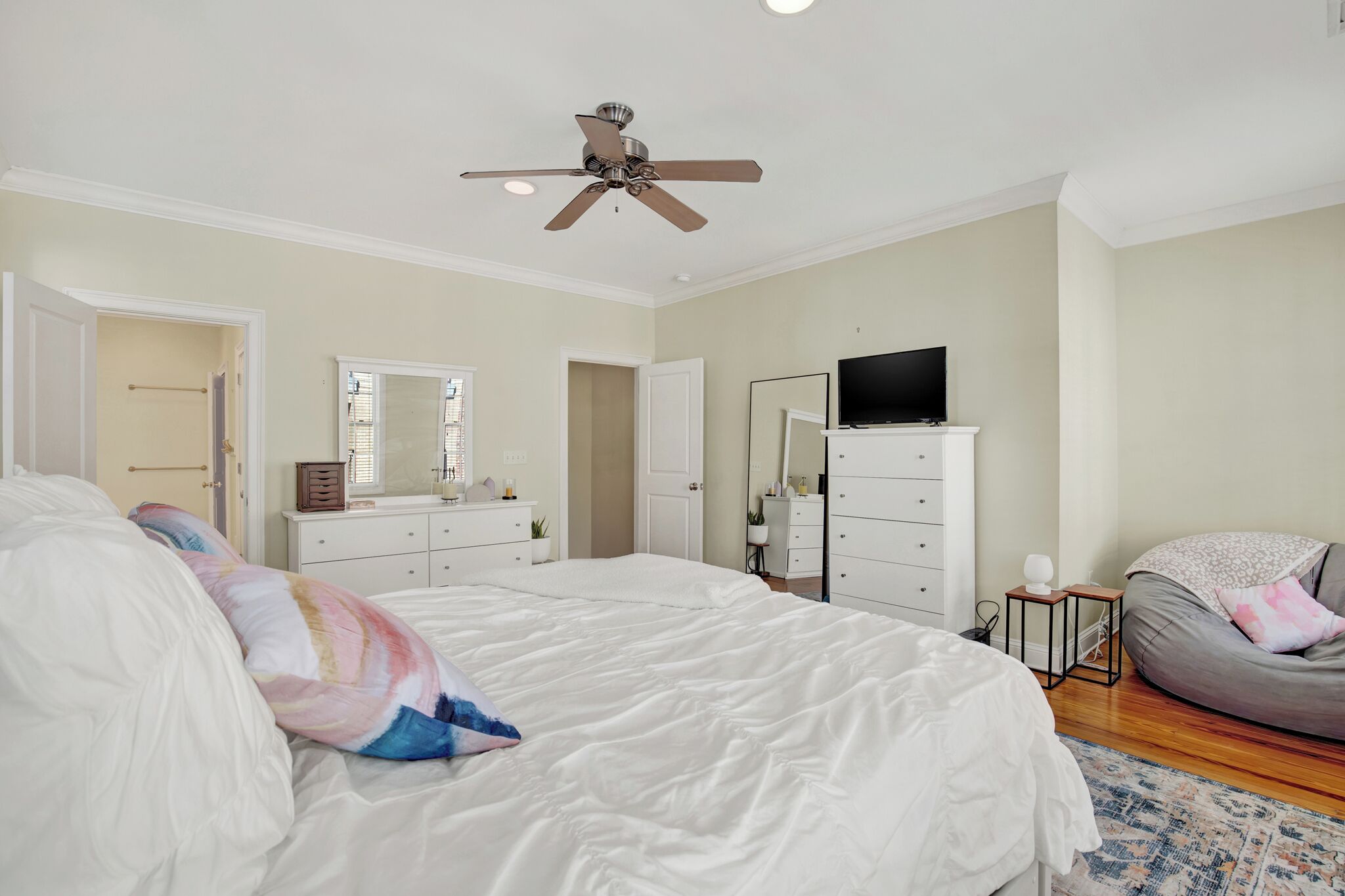 A bedroom with a large bed, a ceiling fan, a TV, a dresser, and a bean bag chair.