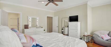 A bedroom with a large bed, a ceiling fan, a TV, a dresser, and a bean bag chair.