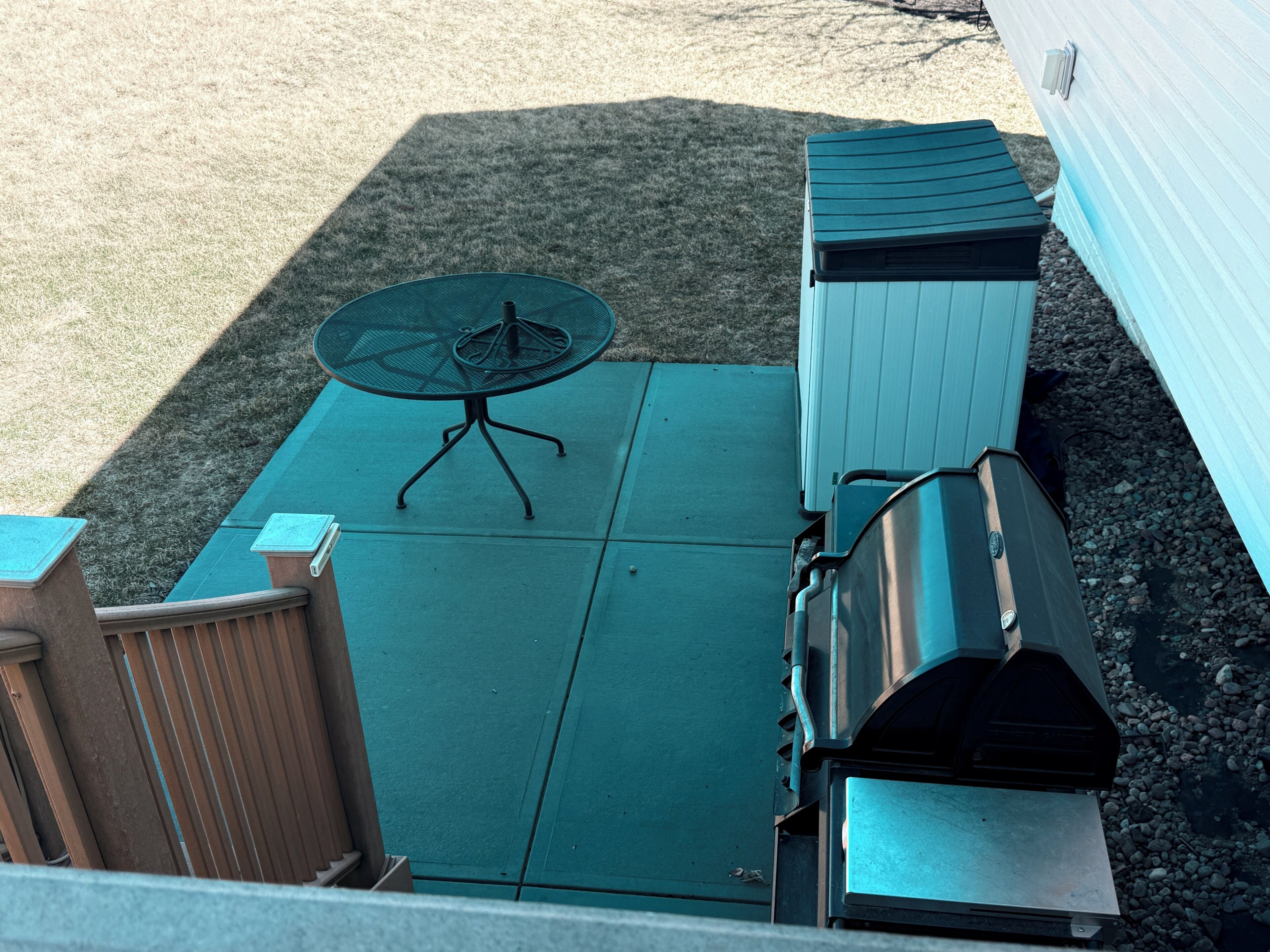 Un patio con una mesa y sillas de metal, una parrilla y un área cercada pequeña.