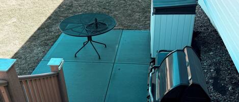 Un patio con una mesa y sillas de metal, una parrilla y un área cercada pequeña.