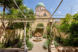 Une cour avec une fontaine, un banc en bois et un bâtiment surmonté d’un dôme.
