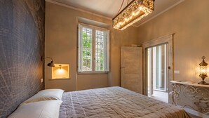 Un dormitorio con cama, ventana con vistas, puerta y lámpara fijada a la pared.