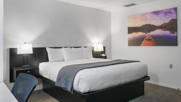 Une chambre d’hôtel avec un lit, des lampes de chevet, un bureau et un tableau représentant un paysage.