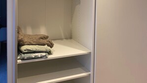 Armário amplo com cabides de madeira e cobertores dobrados nas prateleiras.