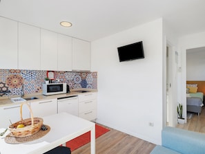 Una cocina compacta con microondas, una cesta de frutas y un televisor montado en la pared.