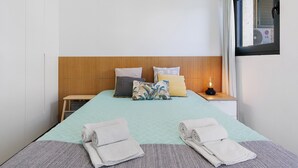 Een hotelkamer met een bed, kussens, een nachtkastje, een lamp en een raam met gordijnen.